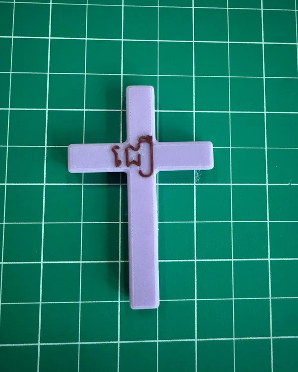 A lavender 3D-printed cross with the Khmer word for "believe" in raised letters at the intersection