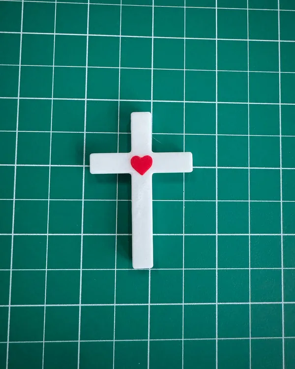A white 3D-printed cross with a small red heart at the intersection
